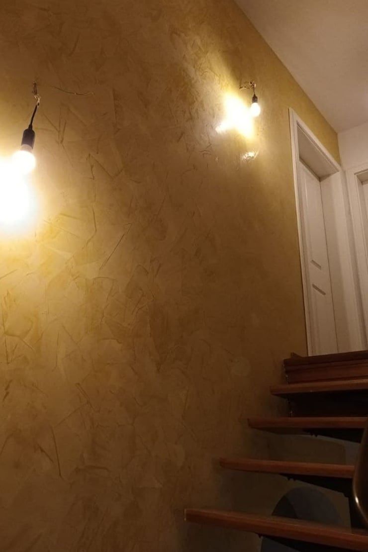 Treppenhaus in einem Altbau mit von Hand aufgezogener Wandfläche in warmem Goldton und originaler Holztreppe