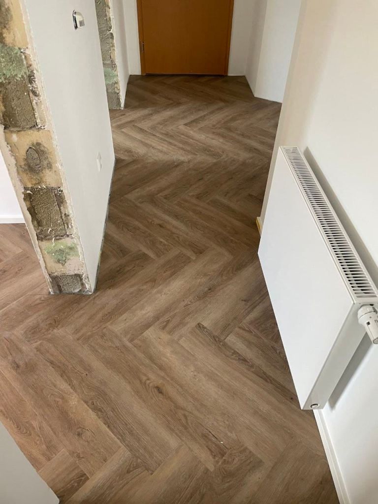 Geöffnete Wandlaibung mit altem Putz und Mauerwerk neben einem fertig verlegten Boden