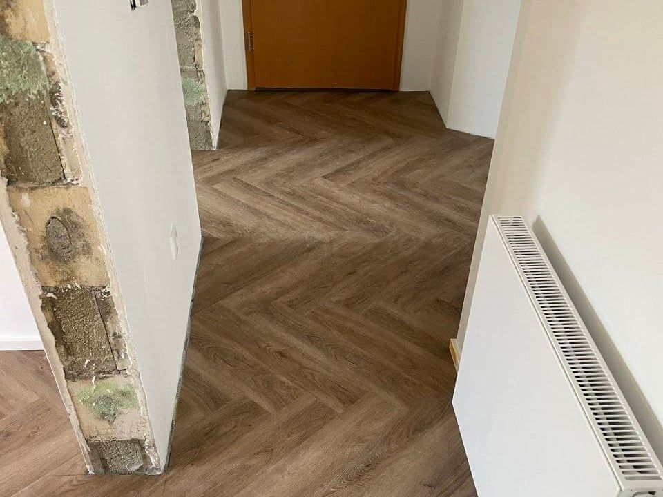 Flur während der Sanierung: links eine geöffnete Wand mit altem Putz und Mauerwerk, rechts der fertig verlegte Fischgrätboden und die gestrichene Wand